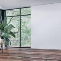 empty unfurnished modern interior with a large potted plant (strelitzia nicolai), a set of lounge yellow chairs and a coffee table in front of large corner windows with garden view and balcony, a blank white wall on the other