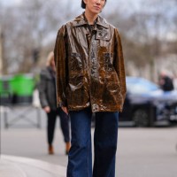 Eva Chen wears a brown shiny leather oversized jacket , blue flared denim pants / jeans , outside Miu Miu , during the Womenswear Fall/Winter...