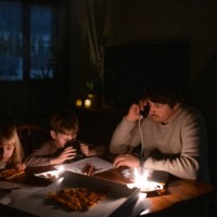 family sitting at home with candles and eating pizza during blackout. children are drawing, man is man is talking by smartphone. energy crisis concept. - junk food stock pictures, royalty-free photos & images