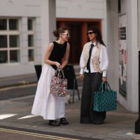Fashion Show Guest was seen wearing black shoes, a colorful bag white wide shorts, a black top and white shades next to a person wearing wide and...