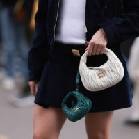Fashion Week Guest is seen wearing a dark blue jacket, with a dark blue skirt, a Miu Miu belt in gold and a white Miu Miu leather Hobo handbag...