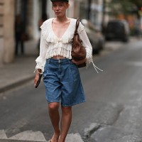 Fashion Week guest is seen wearing a dark grey newsboy cap, a fine silver necklace, a cream-white long-sleeved ruffled blouse with a deep V-neck and...