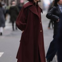 Fashion week guest is seen wearing a long Bordeaux red wool coat with big collar and big sleeves, gold buttons, black tights and black high patent...