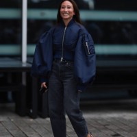 Fashion Week guest is seen wearing a shiny blue cropped bomber jacket with puffy sleeves; grey jeans with straight leg and mid-heeled, pointed, black...