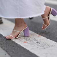 Fashion Week guest is seen wearing an ankle-length white denim skirt with frayed hem, and cream-white leather sandals with two straps and lilac block...
