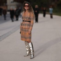 Fashion week guest is seen wearing an orange and green plaid bouclé jacket with a black Chanel belt, a knee-length skirt, silver high boots and brown...