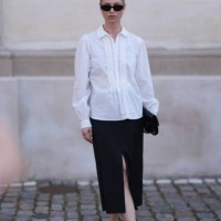 Fashion Week guest is seen wearing oval black sunglasses, silver round earrings, a long-sleeved white blouse with lace details at the chest, collar...