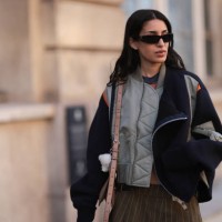 Fashion Week Guest seen wearing a short brown stripped skirt, grey shirt, black sunglasses, black, orange and khaki oversized jacket and a brown Acne...