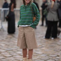 Fashion week guest was seen wearing beige shoes, beige shorts, a brown bag and a green pullover with collar and red stripes before the Loewe Fashion...
