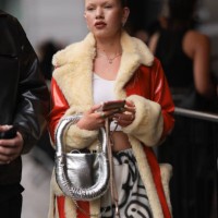 Fashion Week Guest was seen wearing white pants with black writings, a white cropped shirt, a silver bag that is shiny along with lots of jewelry and...