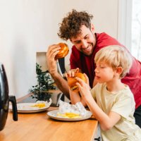 father and son eating hamburger at home - junk food stock pictures, royalty-free photos & images