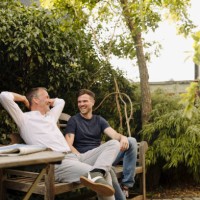 father with hands behind head sitting by son on bench in backyard - garden decoration photos et images de collection