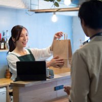 female cafe staff giving a paper bag of take-out food to a male customer - junk food stock pictures, royalty-free photos & images