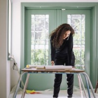 female design professional talking on smart phone while examining blueprints on table at under construction apartment - home decoration stock-fotos und bilder