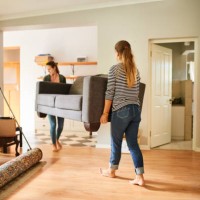 female friends carrying a sofa out of a house on moving day - home decoration stockfoto's en -beelden