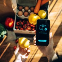 female hands confirming the arrival of a box of home delivery filled with multi-coloured fresh and healthy organic groceries ordered online with mobile app on smartphone. grocery subscription boxes. meal kits. convenient and