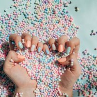 female hands with trendy colorful french manicure are lying on a pastel background, divided into light green and light pink part with many round paper confetti. - nails art stock pictures, royalty-free photos & images