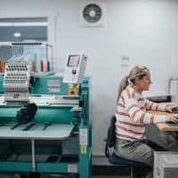 female worker using computer while operating embroidery machine - fashion stock pictures, royalty-free photos & images