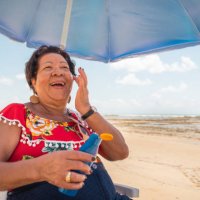 femme aîné utilisant une lotion de bronzage sur la plage - hairstyle photos et images de collection
