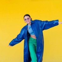 femme élégante posant en manteau bleu, lunettes de soleil foncées sur fond jaune vif, rayonnant de confiance urbaine contemporaine - fashion photos et images de collection