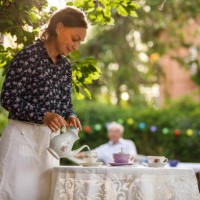 femme mûre heureuse versant du thé dans une tasse de thé sur une table dans la cour arrière - garden decoration photos et images de collection