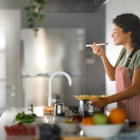 femme souriante appréciant tout en cuisinant des spaghettis pour le déjeuner. - food photos et images de collection