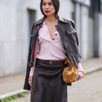 Fernanda Millan wears bright cherry red lipstick, fluffy eyebrows, light pink half unbuttoned long sleeve sweater, shiny black biker leather jacket,...