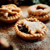 festive scene of 3 home made mince pies dusted with icing sugar on a rustic wooden board with pine cones and holly. - food stock pictures, royalty-free photos & images