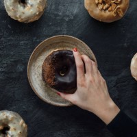 flat lay shot of female hand reaching a variety of gourmet donuts on rustic dark background - junk food stock pictures, royalty-free photos & images