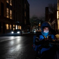 Food delivery driver waits for take-out orders on a quiet street at a shopping mall and restaurant area where inside dining is prohibited and shops...