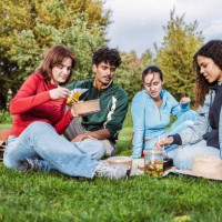 four young people having picnic in the park - junk food stock pictures, royalty-free photos & images