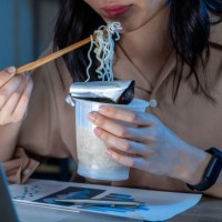 freelance women eating instant noodles while working on laptop in living room at home at night. - junk food stock pictures, royalty-free photos & images