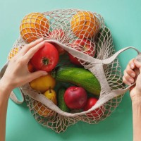 fresh juicy fruits and vegetables, products in a reusable shopping bag. a girl or woman takes or lays out products from a string bag made from recycled materials on a green pastel background. vegetarianism, veganism. no plast