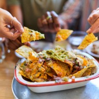 friends sharing nachos with cheese, guacamole and sour cream at restaurant - junk food stock pictures, royalty-free photos & images