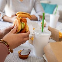 friends smile and laugh while enjoying fast food they had delivered to their home. they're eating burgers and fries - junk food stock pictures, royalty-free photos & images
