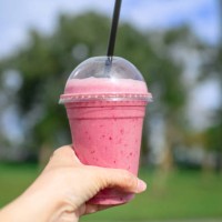 fruit smoothy in plastic take away cup in a woman's hand over city and park background - junk food stock pictures, royalty-free photos & images