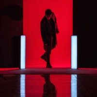 full length of young man standing amidst illuminated lights with reflection on floor in red studio - fashion stock-fotos und bilder
