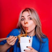 funny woman smeared in sauce sucking noodles from box using chopsticks and look at camera - junk food stock pictures, royalty-free photos & images