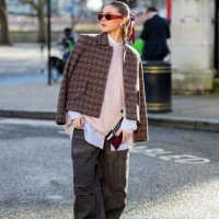 Gabby Martin wears red Prada sunglasses, checkered jacket, oversized knit, grey pants with side pockets outside Holzweiler during London Fashion Week...