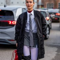 Gabriela Sevillano Fernández wears black bomber coat, red bag, over knees boots, grey tie, button shirt outside Mfpen during the Copenhagen Fashion...