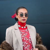 Gabriella Berdugo wears sunglasses, a bejeweled necklace , a red turtleneck pullover with white floral print , a brown fluffy faux fur coat, a beige...