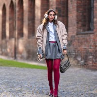Gabriella Berdugo wears white and brown fluffy ear muffs, a beige striped bomber jacket , a white ruffled shirt, a gray blazer jacket , a ruffled...