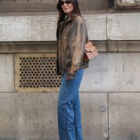 Gala Gonzalez wears black sunglasses, black t-shirt, dark brown light brown pattern oversized leather jacket, navy blue denim jean pants, light green...