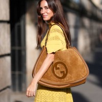 Gala Gonzalez wears dark yellow gold embellished short sleeve corset shirt, shiny dark brown tote leather bag, dark yellow gold embellished midi...