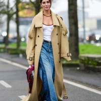Gala Gonzalez wears gold necklace, light yellow Gucci monogram oversized Gucci trench coat, white Gucci tank top, black Gucci leather belt, light...