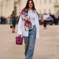 Gala Gonzalez wears white button up long sleeve shirt, navy blue denim jean pants, dark brown leather boots, dark red leather bag, outside Loewe,...