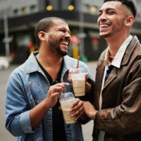 gay friends drinking ice coffee and laughing on a sidewalk in the city - coffee stock pictures, royalty-free photos & images