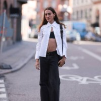 George Gorg is seen wearing golden hoop earrings; a white, long-sleeved shirt with a wide collar that is only buttoned at the top; underneath a black...