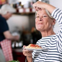 germany, wakendorf, senior woman eating noodles, man cooking in background - food stock pictures, royalty-free photos & images