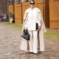 Gili Biegun wears white suit, beige trench coat, black bag, sunglasses and black leather gloves outside the Munthe fashion show during the Copenhagen...